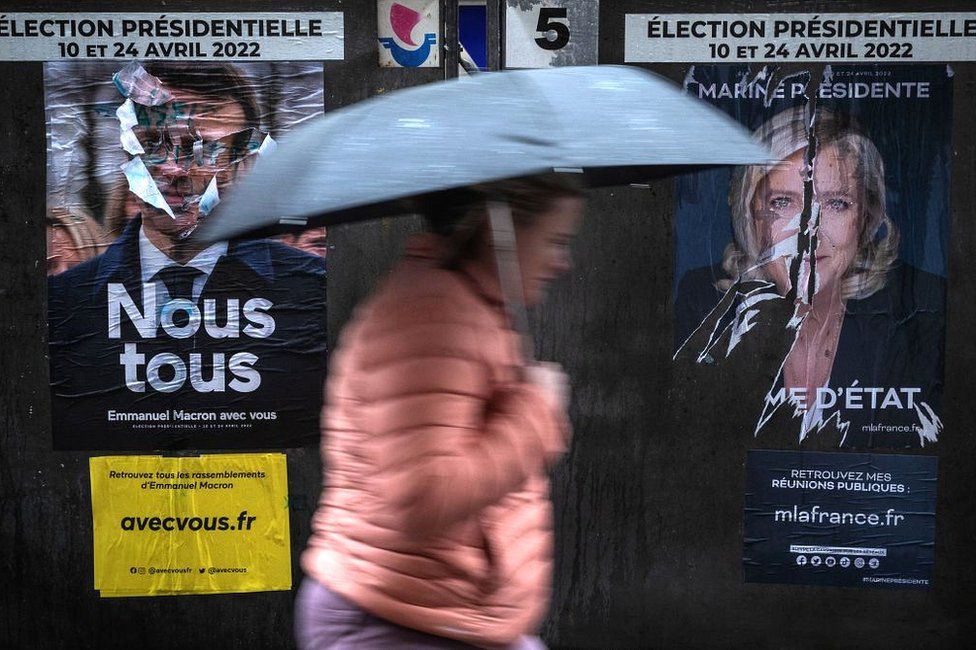 A woman walks past campaign posters in Paris on 8 April 2022