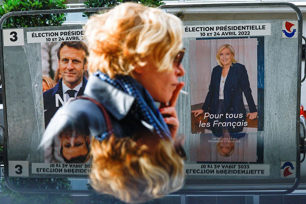 A woman walks past official campaign posters of presidential election candidates President Emmanuel Macron and Marine le Pen in Paris, on 19 April 2022