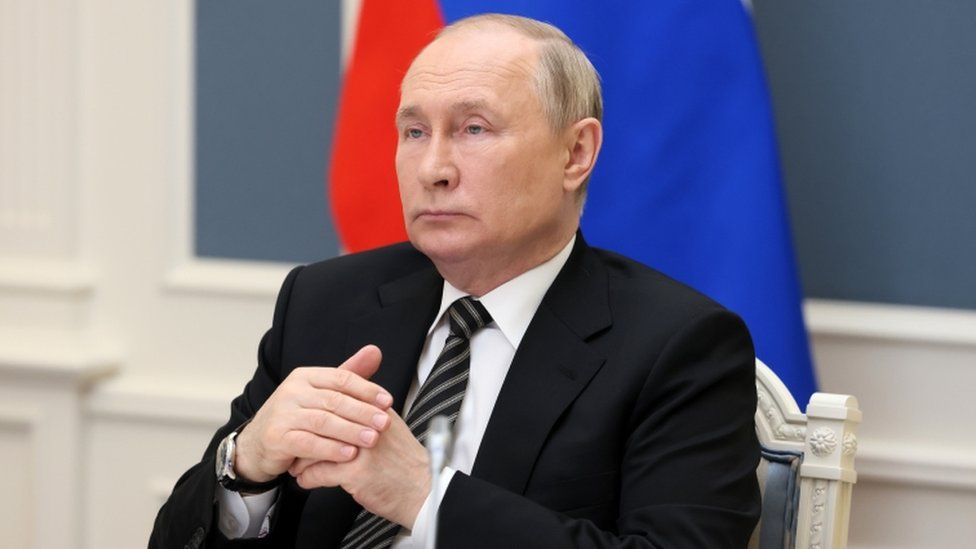Russian President Vladimir Putin sits opposite a Russian flag