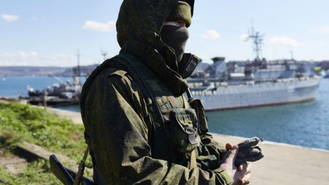 A Russian soldier stands in front of a naval vessel in the Crimea