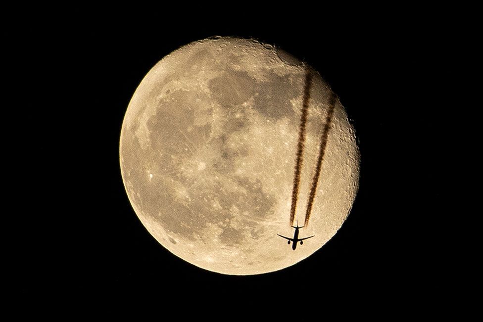 An aircraft flies above Basra, in southern Iraq, silhouetted against the waning gibbous moon on 18 April 2022